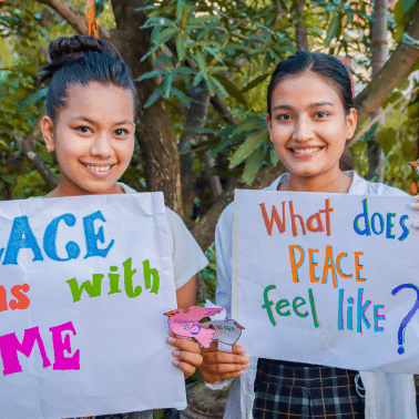 Two Nepalese young women hold signs saying 'peace begins with me' and are smiling