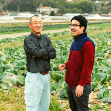 An older and younger Asian male laugh easily in a field of cabbages