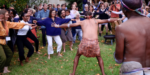 Crowd gathered with arms outstretched around an Aboriginal man